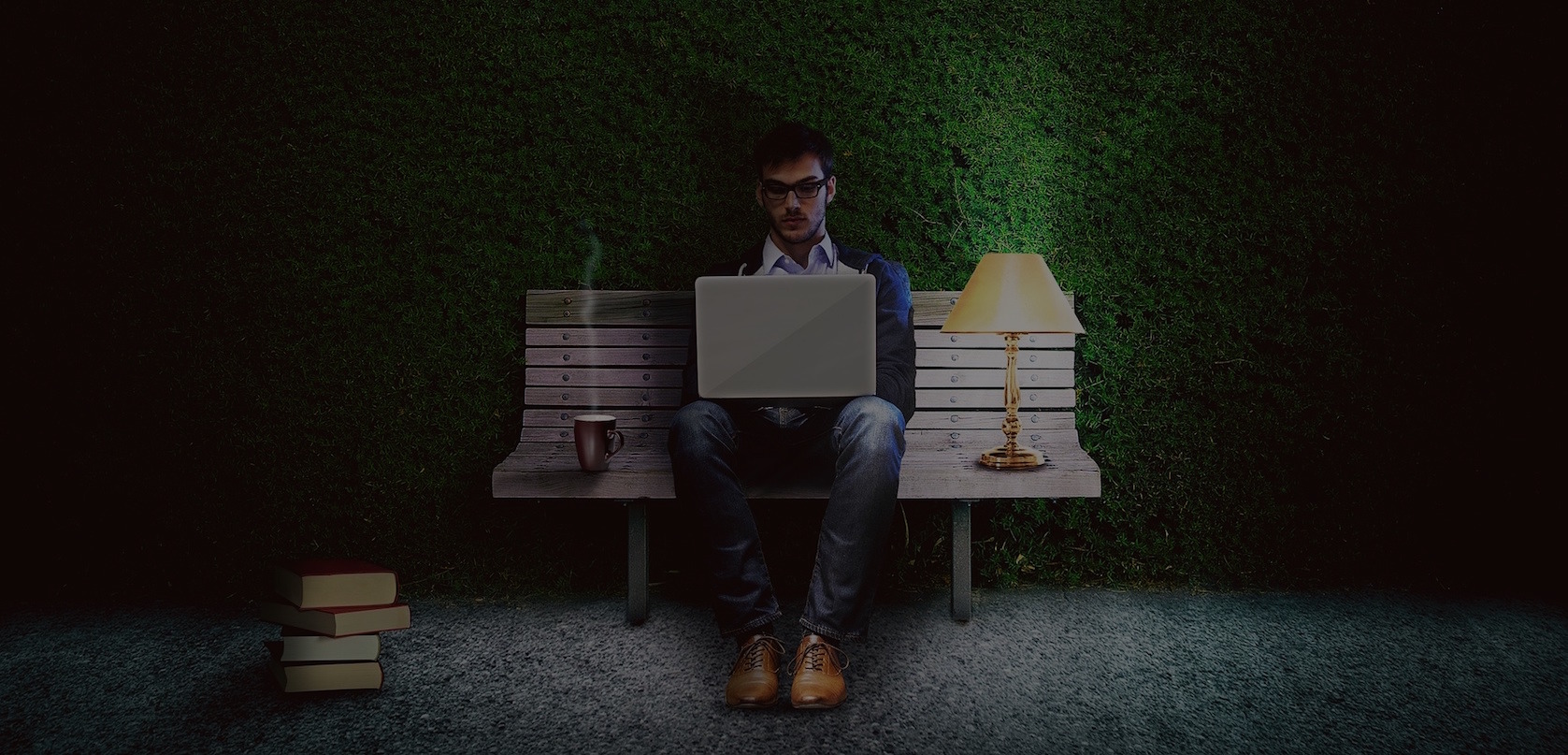 Man sitting on a bench in front of dark maze wall, writing code on a MacBook